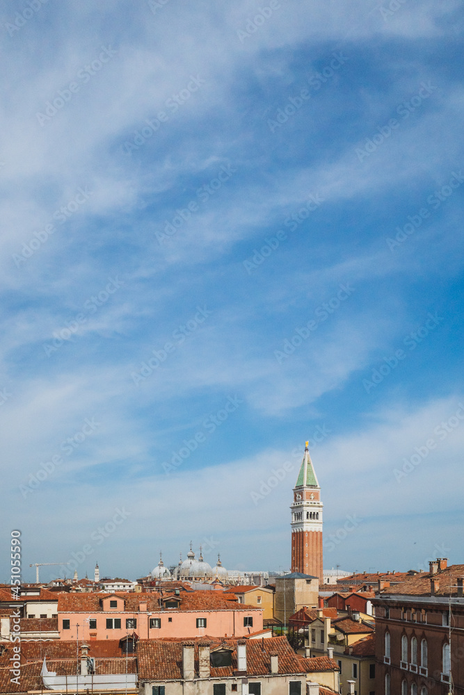 San Marco bell tower over traditional Venetian houses under blue sky in Venice, Italy