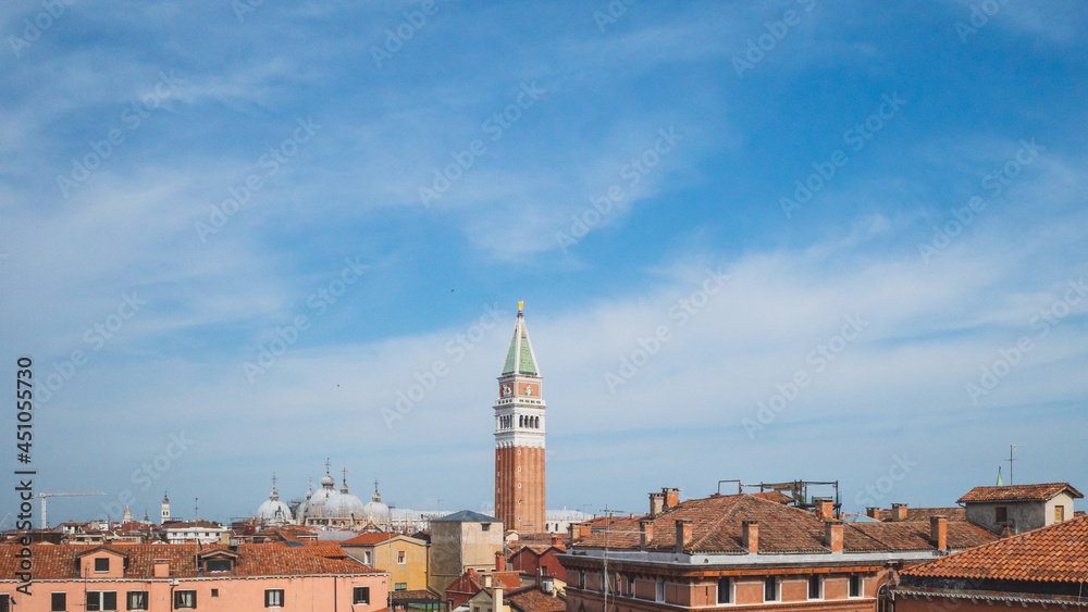 Fototapeta premium San Marco bell tower over traditional Venetian houses under blue sky in Venice, Italy