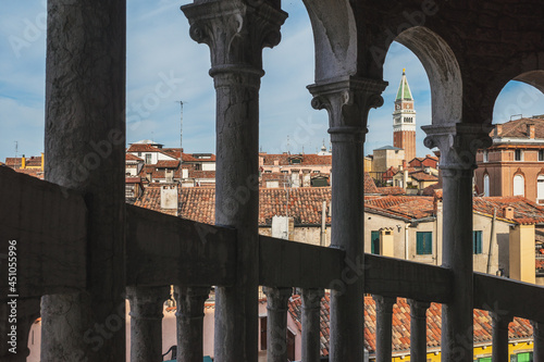 San Marco bell tower over traditional Venetian houses viewed between columns in Venice, Italy