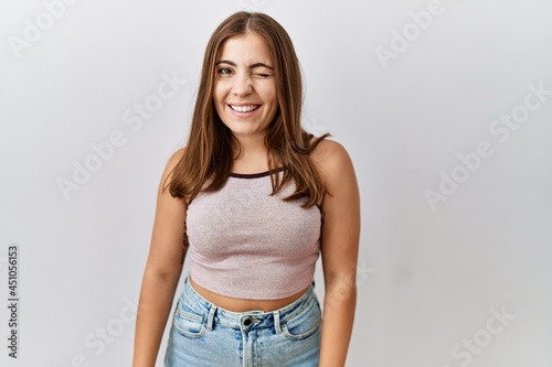 Young brunette woman standing over isolated background winking looking at the camera with sexy expression, cheerful and happy face.