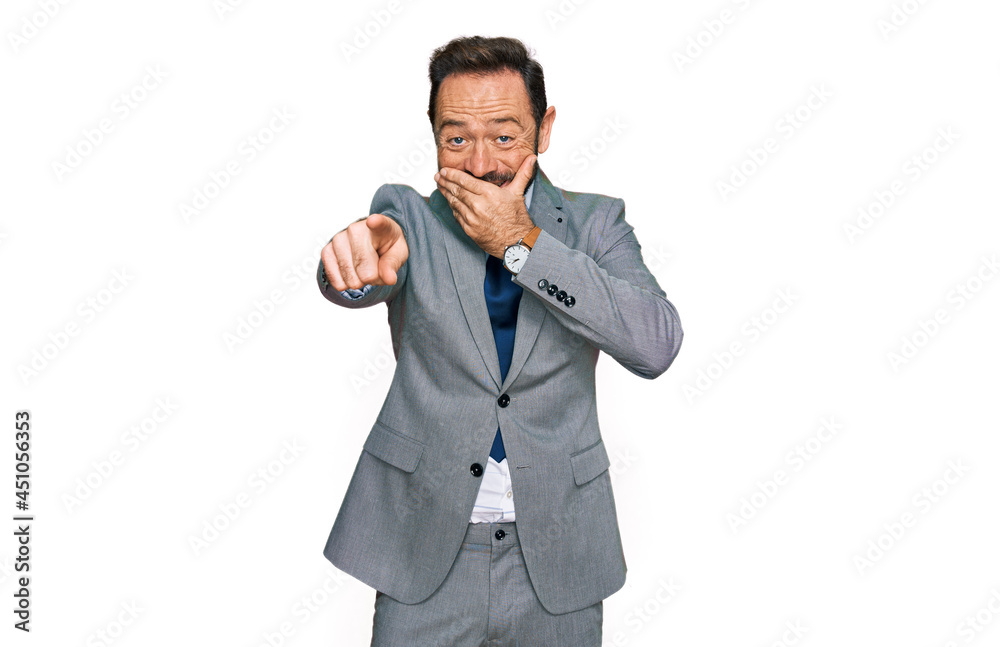 Middle age man wearing business clothes laughing at you, pointing finger to the camera with hand over mouth, shame expression Middle age man wearing business clothes laughing at you, pointing finger to the camera with hand over mouth, shame expression