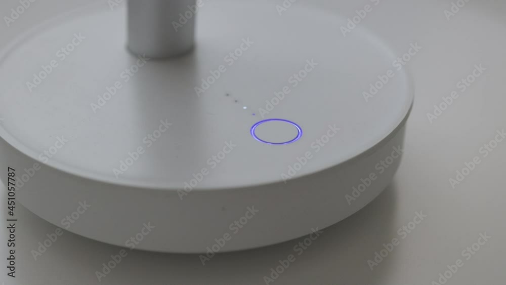 Close-up of pushing a button to turn on and off with indicator blue light the air white electric cooling fan. Fingers press the power switch Close-up of pushing a button to turn on and off with indicator blue light the air white electric cooling fan. Fingers press the power switch