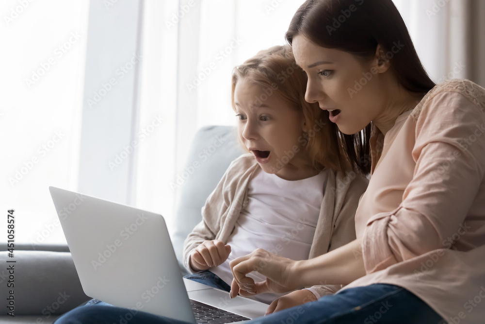 Stunned young mother and small teen daughter use laptop look at screen shocked by unexpected news online. Amazed mom and little daughter surprised by online sale deal or promotion discount on web.