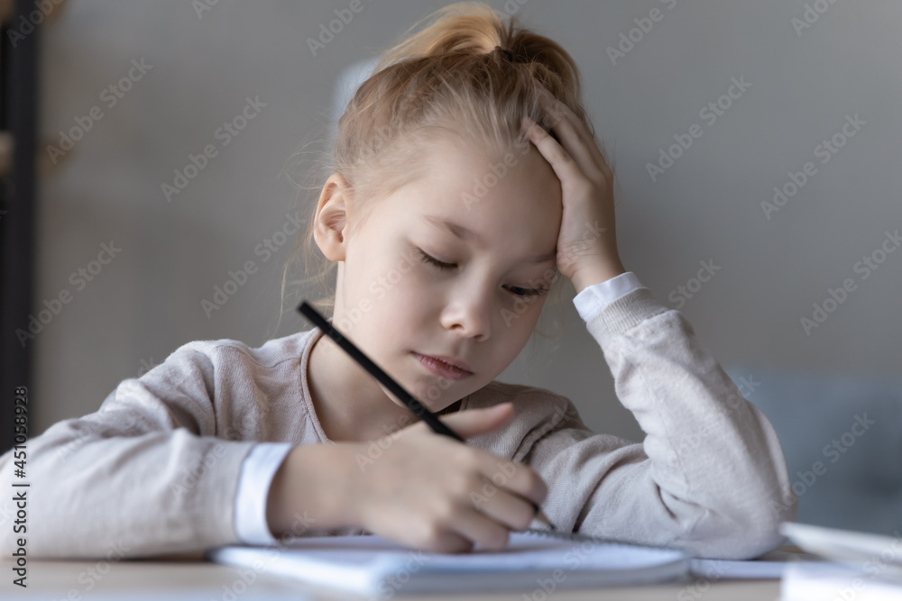 Unhappy small kid sit at desk at home handwrite in notebook lack motivation prepare homework for school. Sad little girl child feel lazy unmotivated doing task assignment. Education concept. Unhappy small kid sit at desk at home handwrite in notebook lack motivation prepare homework for school. Sad little girl child feel lazy unmotivated doing task assignment. Education concept.