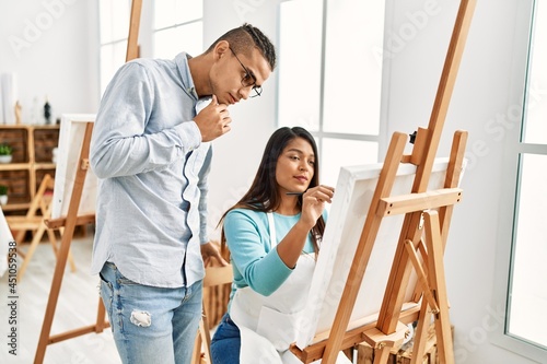 Young latin painter couple with serious expression painting at art studio