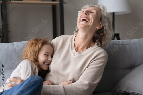 Overjoyed old Caucasian 60s grandmother and small teen granddaughter have fun laugh and joke together. Smiling mature grandma and little grandchild play enjoy leisure funny weekend at home.