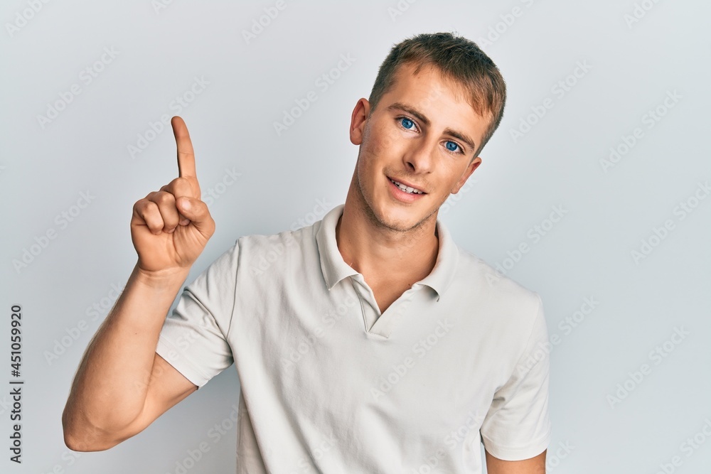 Young caucasian man wearing casual white polo smiling with an idea or question pointing finger up with happy face, number one Young caucasian man wearing casual white polo smiling with an idea or question pointing finger up with happy face, number one