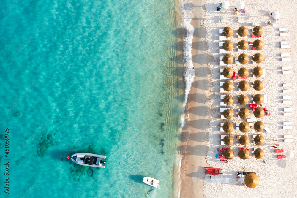 View from above, stunning aerial view of a beautiful beach bathed by a turquoise water and some beach umbrellas illuminated at sunset. Cala di volpe beach,Sardinia, Italy.