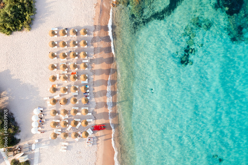 View from above, stunning aerial view of a beautiful beach bathed by a turquoise water and some beach umbrellas illuminated at sunset. Cala di volpe beach,Sardinia, Italy.