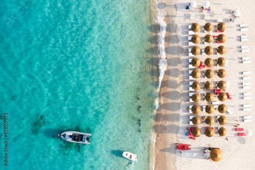 Obraz na płótnie View from above, stunning aerial view of a beautiful beach bathed by a turquoise water and some beach umbrellas illuminated at sunset. Cala di volpe beach,Sardinia, Italy. w salonie