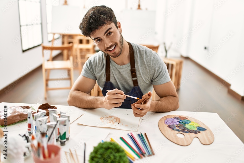 Young hispanic artist man smiling happy painting pottery at art studio. Young hispanic artist man smiling happy painting pottery at art studio.