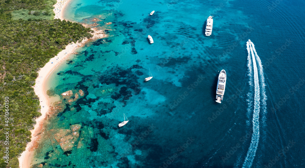 View from above, stunning aerial view of a green coastline with a white sand beach and and boats sailing on a turquoise water at sunset. Cala di volpe beach,Sardinia, Italy.