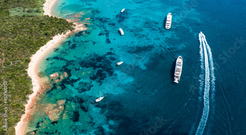 Obraz na płótnie View from above, stunning aerial view of a green coastline with a white sand beach and and boats sailing on a turquoise water at sunset. Cala di volpe beach,Sardinia, Italy. w salonie