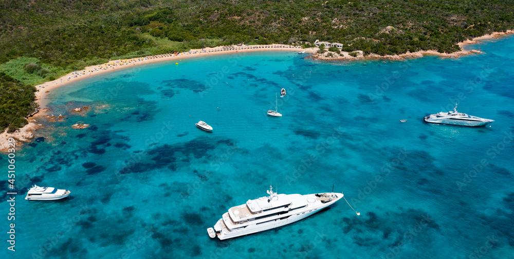 View from above, stunning aerial view of a green coastline with a white sand beach and and boats sailing on a turquoise water at sunset. Cala di volpe beach,Sardinia, Italy.
