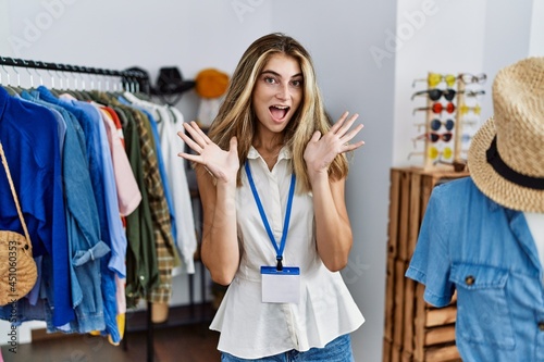 Young blonde woman working as manager at retail boutique celebrating crazy and amazed for success with arms raised and open eyes screaming excited. winner concept