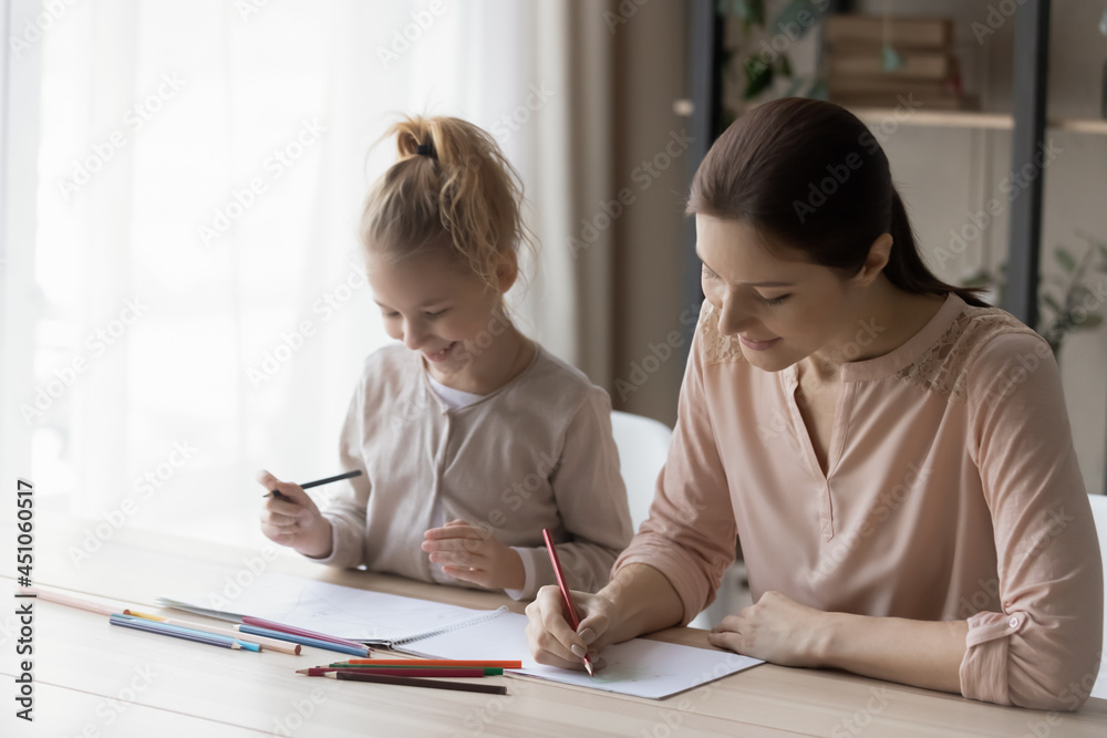 Happy loving young Caucasian mother and small teen daughter sit at desk draw paint together in album. Smiling caring mom and little girl child enjoy artistic activity relaxing. Art, hobby concept. Happy loving young Caucasian mother and small teen daughter sit at desk draw paint together in album. Smiling caring mom and little girl child enjoy artistic activity relaxing. Art, hobby concept.