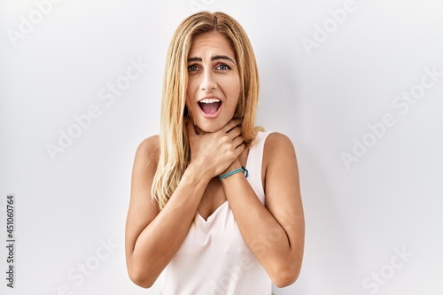 Blonde beautiful young woman standing over white isolated background shouting and suffocate because painful strangle. health problem. asphyxiate and suicide concept.