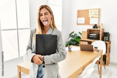 Blonde business woman at the office sticking tongue out happy with funny expression. emotion concept.