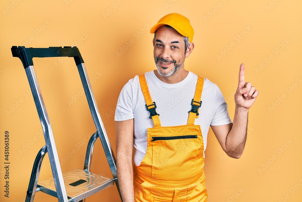 Handsome middle age man with grey hair holding ladder showing and pointing up with finger number one while smiling confident and happy. Handsome middle age man with grey hair holding ladder showing and pointing up with finger number one while smiling confident and happy.