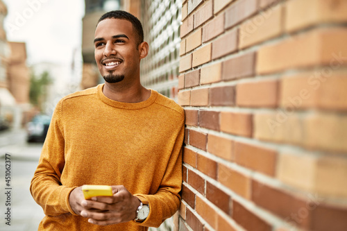 Young african american man smiling happy using smartphone at the city.