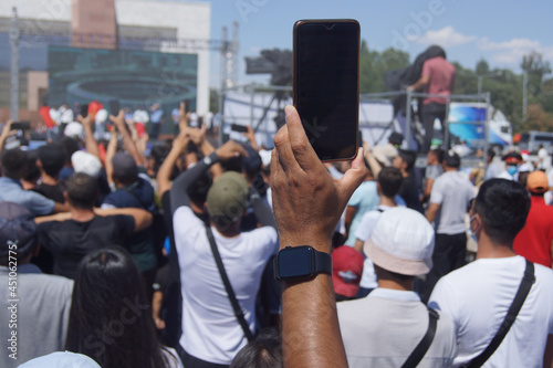 A crowd of people and police in the shade at a rally under the flag of Kyrgyzstan.