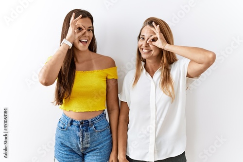 Mother and daughter together standing together over isolated background doing ok gesture with hand smiling, eye looking through fingers with happy face.