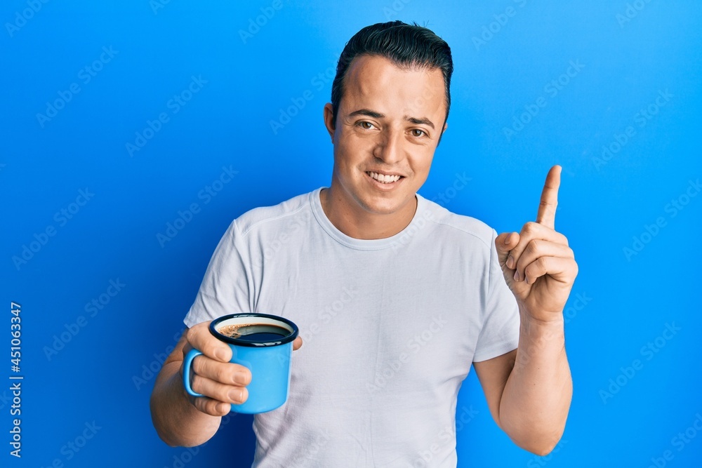 Handsome young man drinking a cup coffee smiling with an idea or question pointing finger with happy face, number one Handsome young man drinking a cup coffee smiling with an idea or question pointing finger with happy face, number one