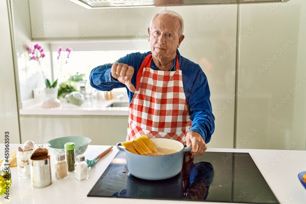 Senior man with grey hair cooking spaghetti at home kitchen with angry face, negative sign showing dislike with thumbs down, rejection concept Senior man with grey hair cooking spaghetti at home kitchen with angry face, negative sign showing dislike with thumbs down, rejection concept