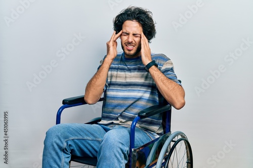 Handsome hispanic man sitting on wheelchair with hand on head, headache because stress. suffering migraine.