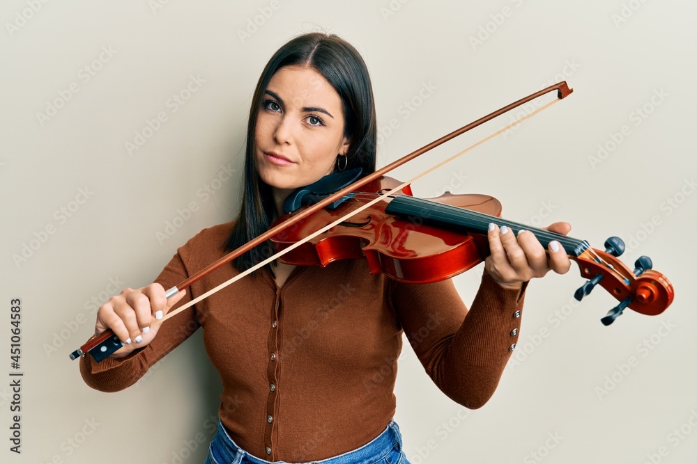 Young brunette woman playing violin relaxed with serious expression on face. simple and natural looking at the camera. Young brunette woman playing violin relaxed with serious expression on face. simple and natural looking at the camera.