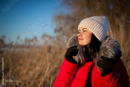 a series of photographs with a young woman in the winter forest. girl in a snowy park. in a red jacket on the banks of a frozen river. winter walk in nature. Cold season. Beautiful girl, sunny day.