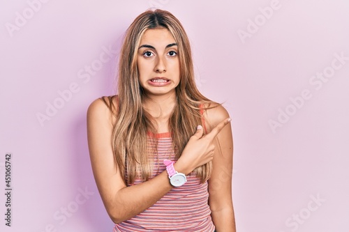 Beautiful hispanic woman wearing casual summer t shirt pointing aside worried and nervous with forefinger  concerned and surprised expression