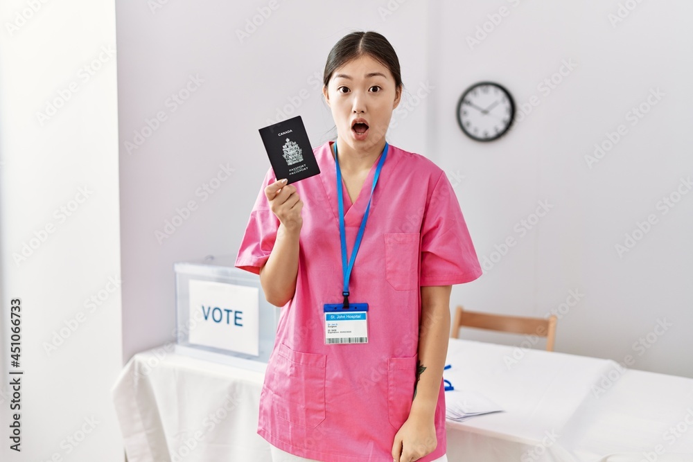 Young asian nurse woman at political campaign election holding canada passport scared and amazed with open mouth for surprise, disbelief face Young asian nurse woman at political campaign election holding canada passport scared and amazed with open mouth for surprise, disbelief face