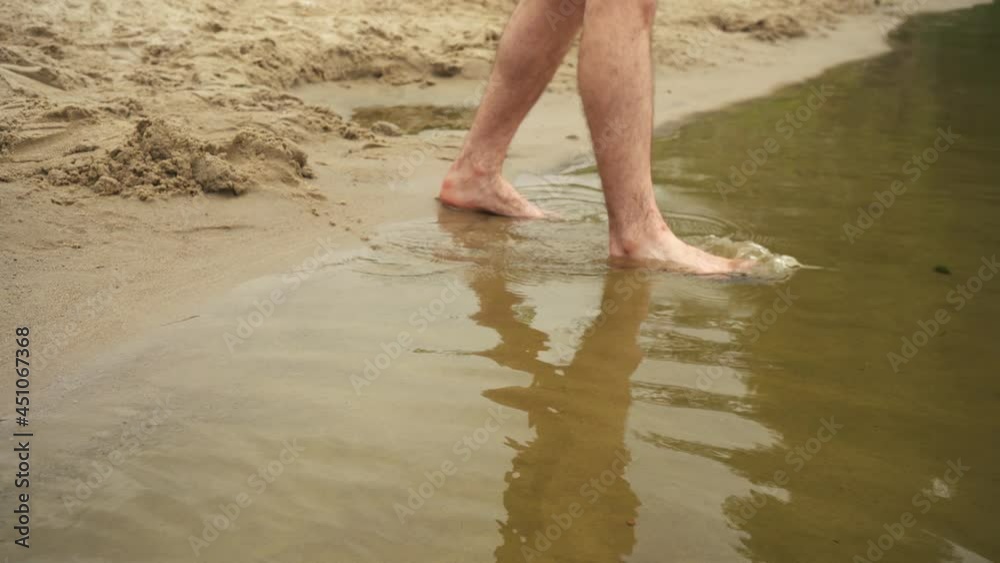 a man walks into the river with bare feet on a sandy beach a man walks into the river with bare feet on a sandy beach