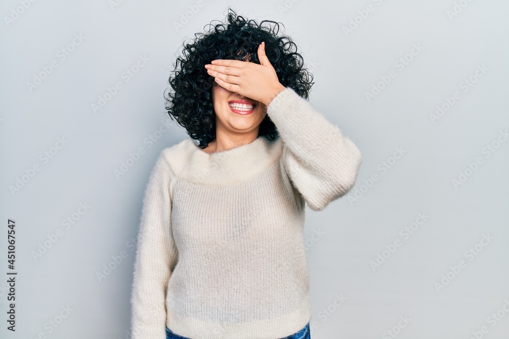 Young middle east woman wearing casual white tshirt smiling and laughing with hand on face covering eyes for surprise. blind concept. Young middle east woman wearing casual white tshirt smiling and laughing with hand on face covering eyes for surprise. blind concept.