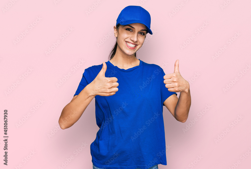 Young hispanic girl wearing delivery courier uniform success sign doing positive gesture with hand, thumbs up smiling and happy. cheerful expression and winner gesture.