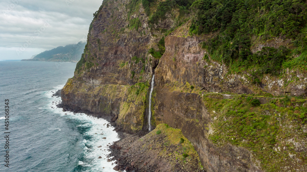 Waterfall falling into ocean from volcanic cliffs.