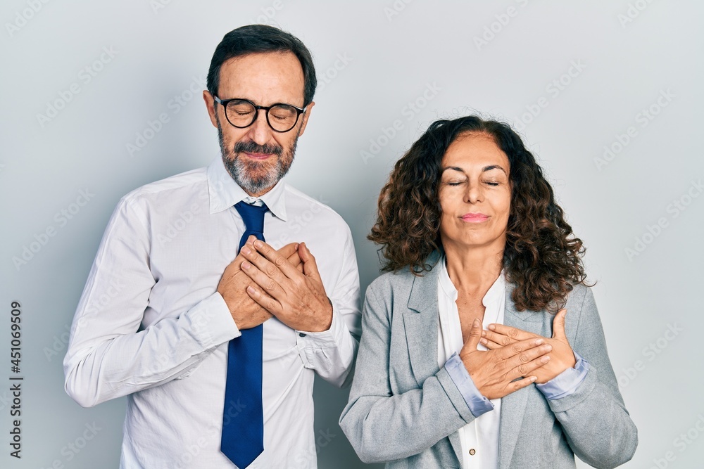 Middle age couple of hispanic woman and man wearing business office uniform smiling with hands on chest with closed eyes and grateful gesture on face. health concept. Middle age couple of hispanic woman and man wearing business office uniform smiling with hands on chest with closed eyes and grateful gesture on face. health concept.