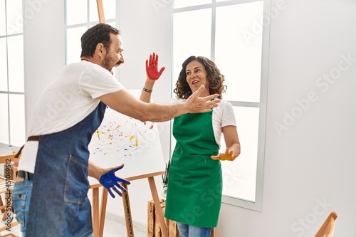 Two middle age student smiling happy playing with paint hands at art studio.