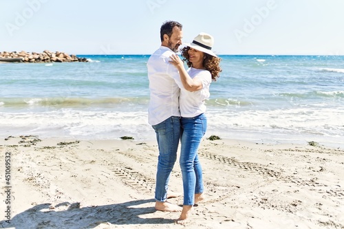 Middle age hispanic couple smiling happy dancing at the beach.