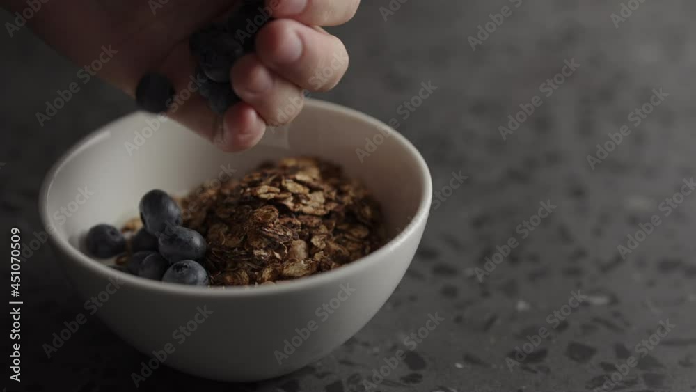 Slow motion add blueberries to granola with yogurt in white bowl Slow motion add blueberries to granola with yogurt in white bowl