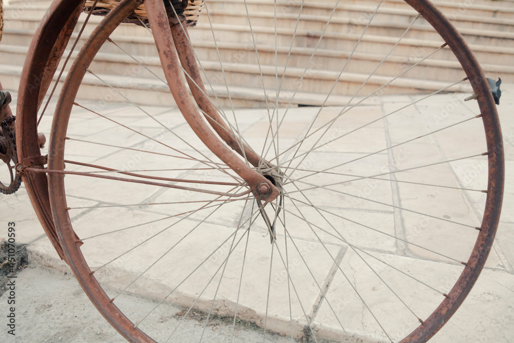 The wheel of a rusty old bicycle, without the tire. Daylight exterior detail shot.
