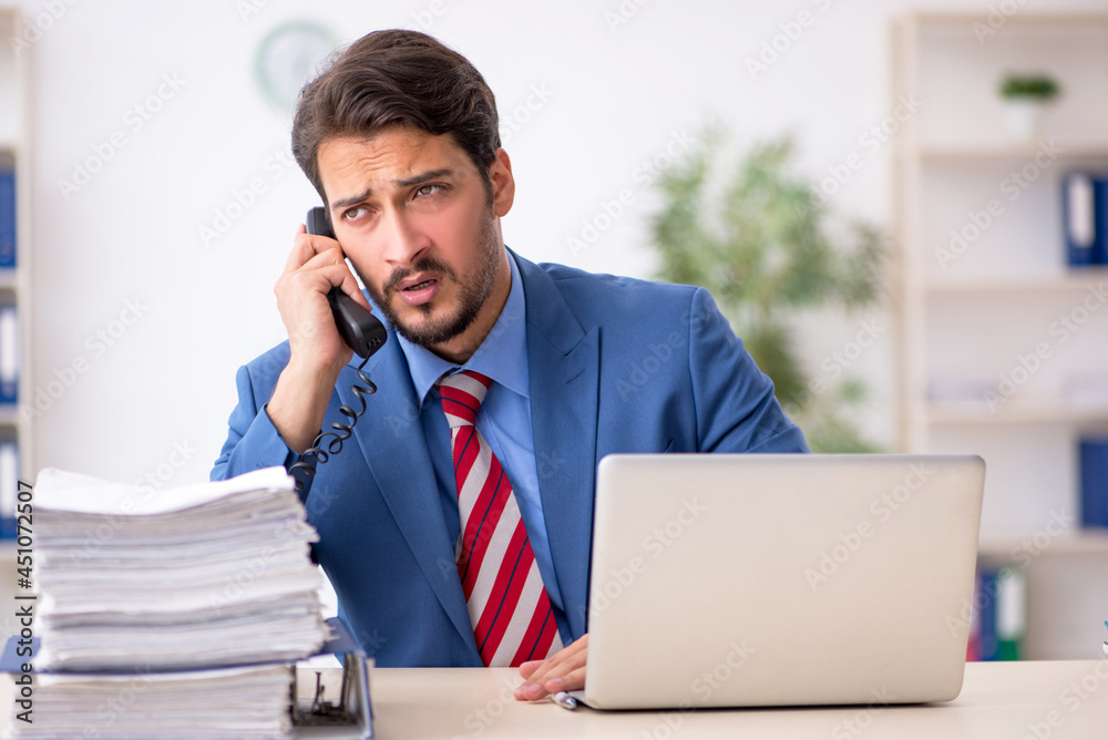 Young male employee unhappy with excessive work in the office Young male employee unhappy with excessive work in the office