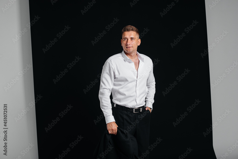 A handsome young man takes off his jacket and laughs posing on a black background. A stylish business man. A big businessman.