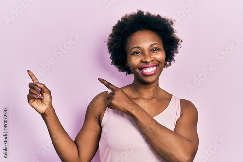 Young african american woman wearing casual sleeveless t shirt smiling and looking at the camera pointing with two hands and fingers to the side.