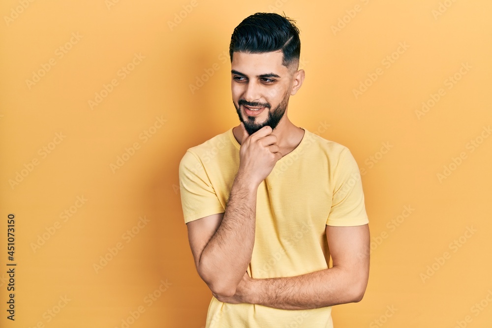 Handsome man with beard wearing casual yellow t shirt with hand on chin thinking about question, pensive expression. smiling with thoughtful face. doubt concept. Handsome man with beard wearing casual yellow t shirt with hand on chin thinking about question, pensive expression. smiling with thoughtful face. doubt concept.
