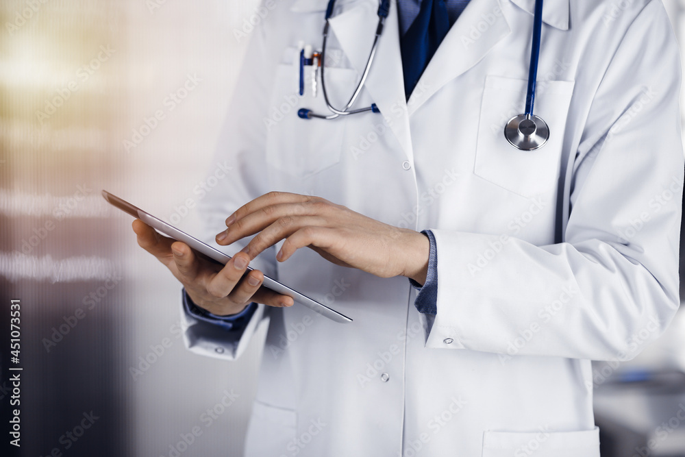 Unknown male doctor using tablet computer in sunny clinic, closeup. Perfect medical service in hospital. Medicine and healthcare concept Unknown male doctor using tablet computer in sunny clinic, closeup. Perfect medical service in hospital. Medicine and healthcare concept