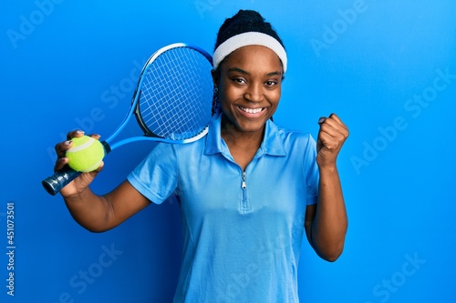 African american woman with braided hair playing tennis holding racket and ball screaming proud, celebrating victory and success very excited with raised arm © Krakenimages.com