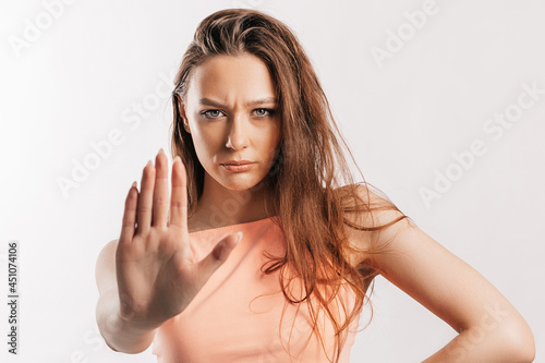 Stop. Enough. Young beautiful girl stretches out her hand to the camera to stop the effect. Woman with fashion orange top on an isolated gray background. Bad events, despair and threat