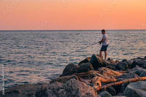 Active recreation in nature. A man with a fishing rod is fishing on the rocks near the sea. A fisherman catches fish at sunset.